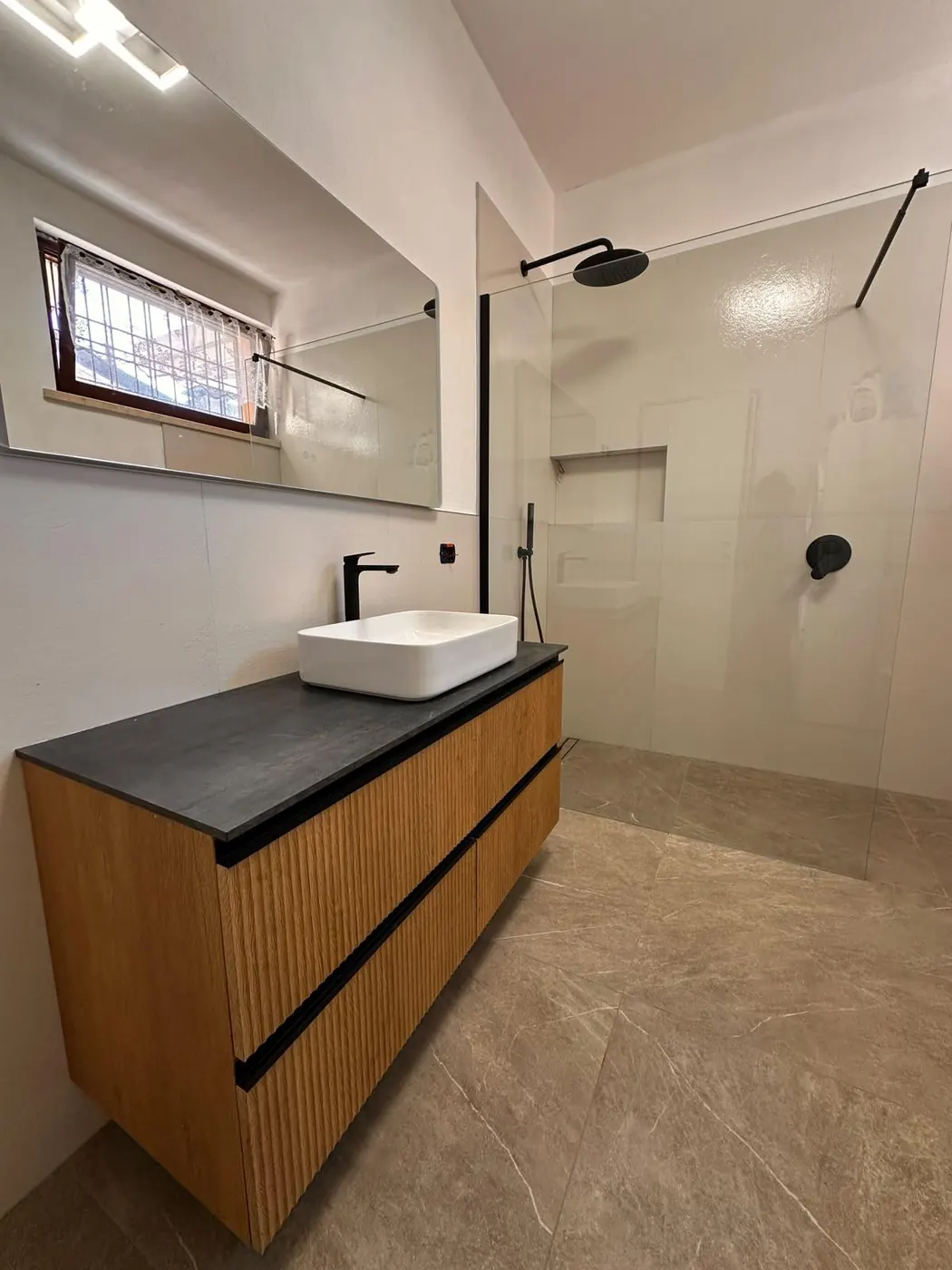 Lo stesso bagno ristrutturato, con mobile in legno e doccia con finiture nere